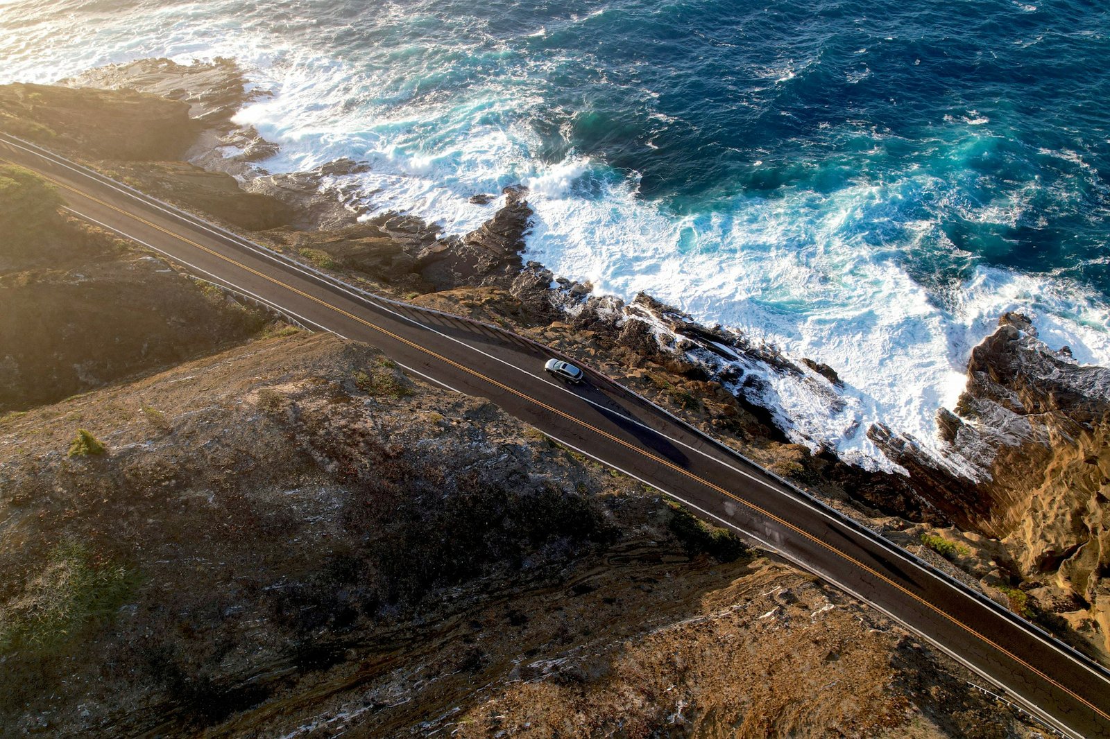 A car following a scenic coastal road beside turquoise ocean waves